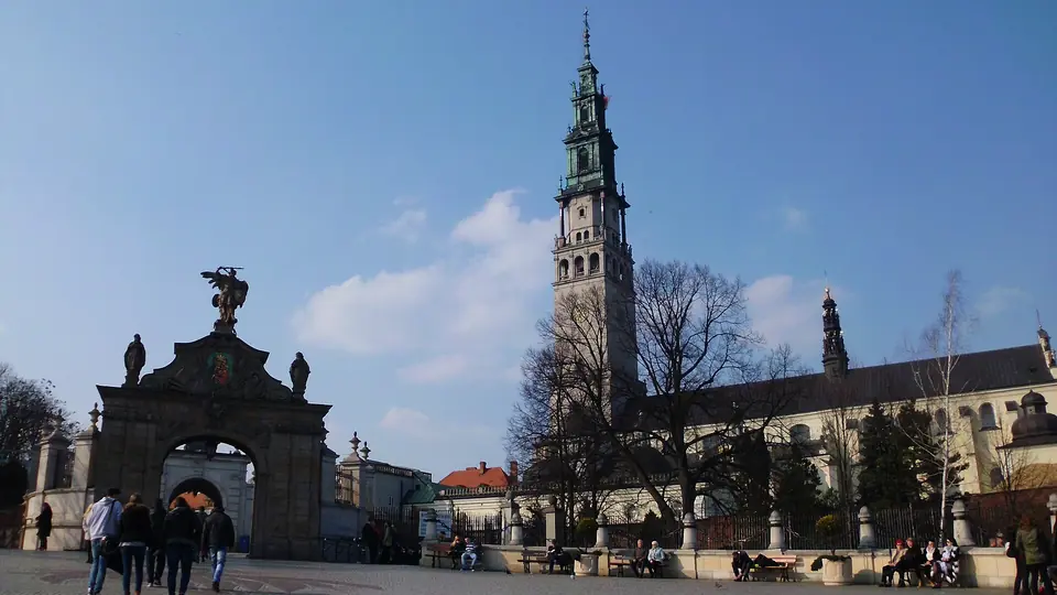 Klasztor na Jasnej Górze w Częstochowie z wysoką wieżą i bramą, przed nim przechodnie