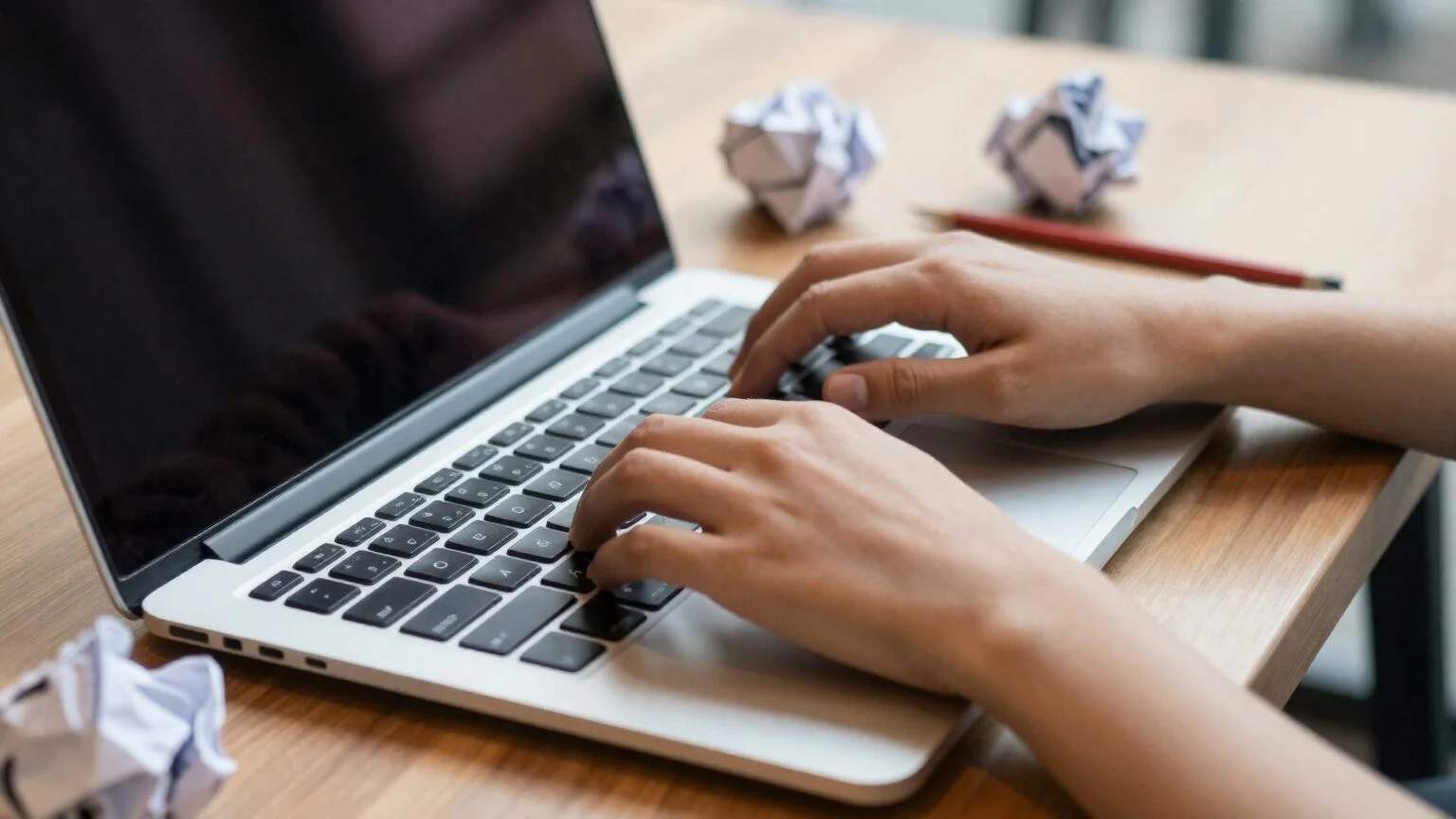 Hands typing on a laptop at a café table, next to crumpled pages with draft versions of the copy