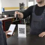 Klient warsztatu skanuje kod QR z linkiem do opinii Google przy ladzie